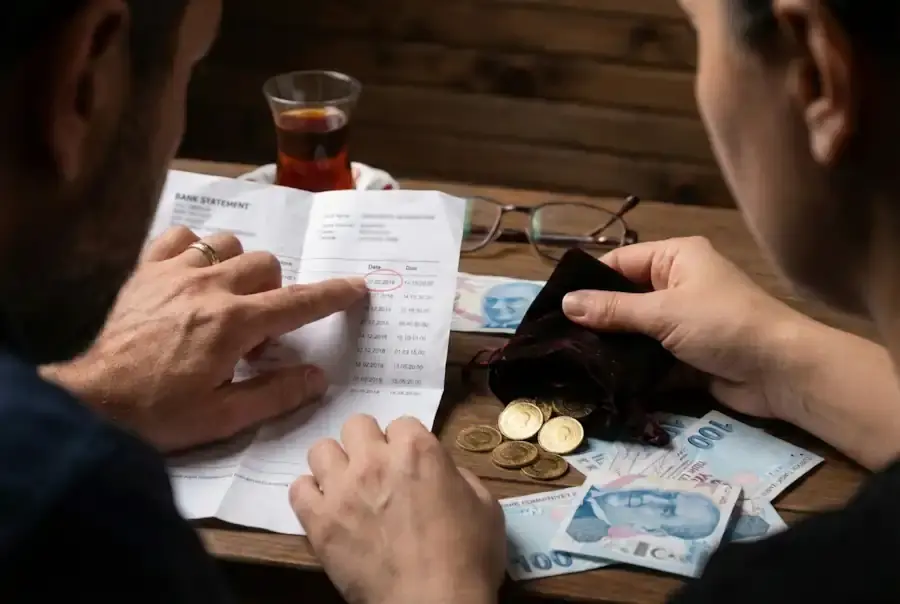 Close-up of hands analyzing bank statements and Turkish Lira coins to calculate mortgage contribution claims and financial evidence for Turkish Family Court.