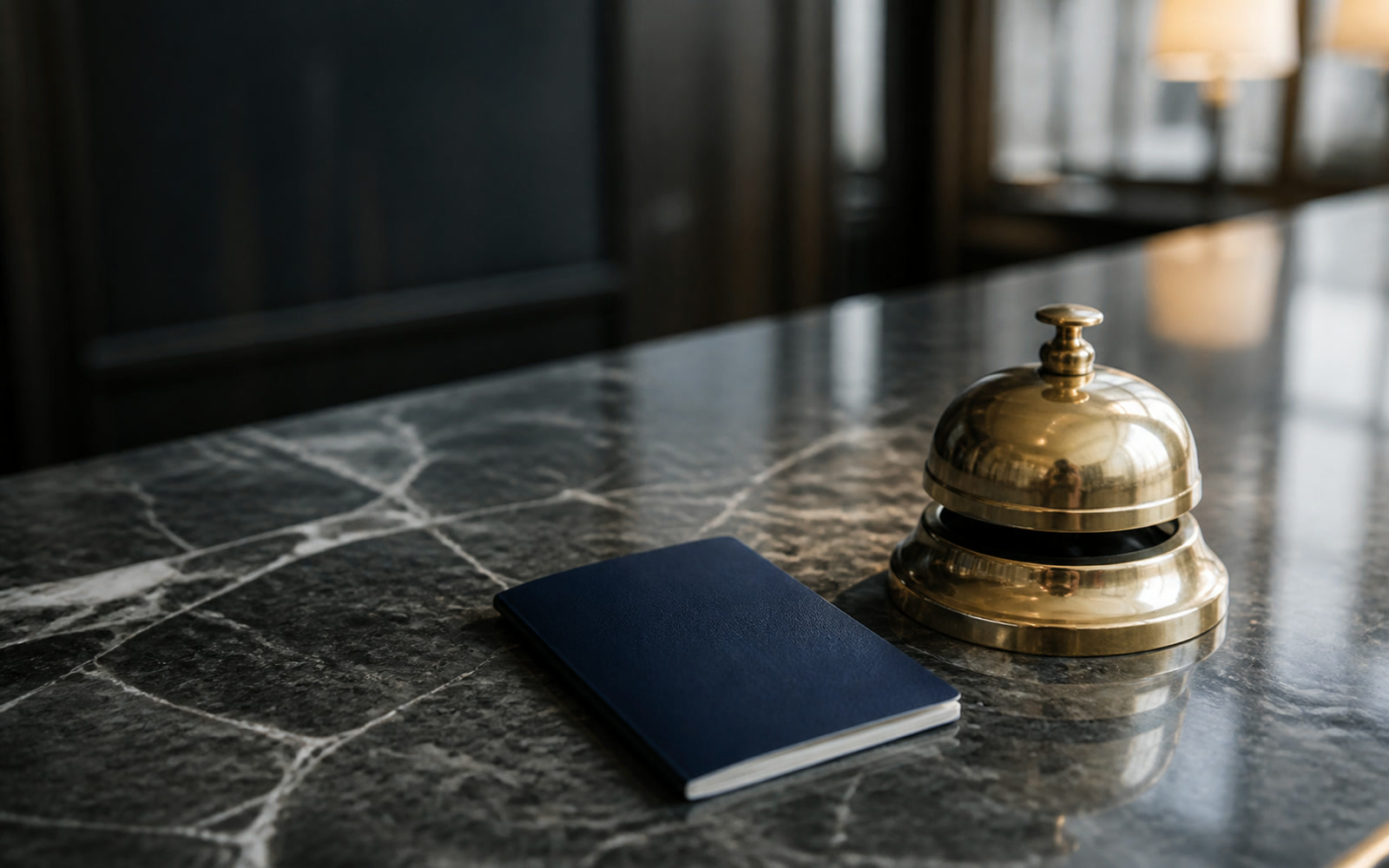 A passport lying closed on a marble counter beside a brass desk bell